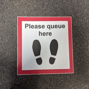 a square floor sticker informing customers where to stand when waiting